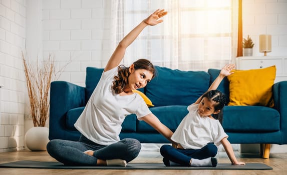 A mother supports her daughter during family yoga focusing on stretch and balance. Their smiles create a heartwarming and harmonious moment at home.