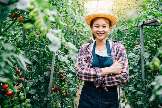 In a greenhouse, a smiling farm owner stands by ripe green tomatoes with crossed arms. The portrait signifies success, happiness, and expertise in vegetable farming and entrepreneurship.