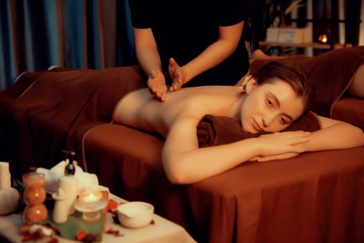 Caucasian couple customer enjoying relaxing anti-stress spa massage and pampering with beauty skin recreation leisure in warm candle lighting ambient salon spa at luxury resort or hotel. Quiescent