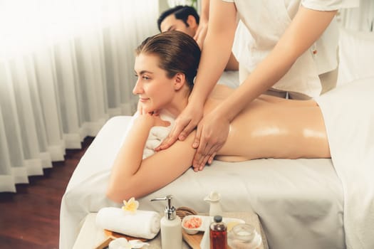 Caucasian couple customer enjoying relaxing anti-stress spa massage and pampering with beauty skin recreation leisure in day light ambient salon spa at luxury resort or hotel. Quiescent