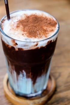 Iced chocolate with whipped cream and cocoa powder on wooden table.