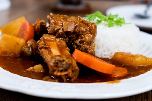 Curry pork with rice in a white plate on a wooden table