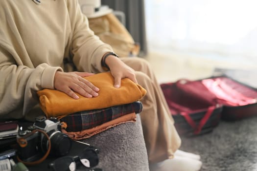 Cropped shot young woman sitting on couch packing suitcase for vacations trip