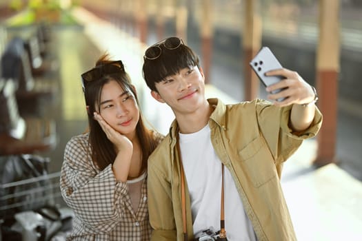 Young tourist couple taking a selfie while waiting for train in railway station platform.