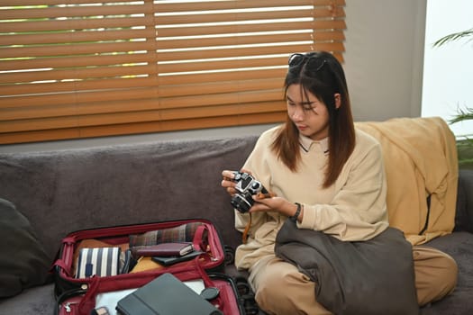 Young woman getting ready to travel vacation, packing suitcase with clothes and accessories in living room.