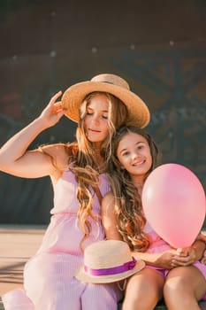 Portrait of mother and daughter in pink dresses with flowing long hair against the black backdrop. The woman hugs and presses the girl to her