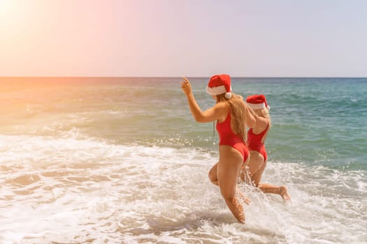 Women in Santa Claus hats run into the sea dressed in red swimsuits. Celebrating the New Year in a hot country.