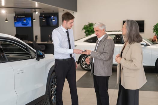 A salesman hands over the keys to a new car to an elderly Caucasian couple