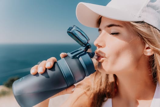 Fintess woman drinking water. Happy, active middle aged woman standing on beach and drinking water after excersise. Concept of lifestyle, sport. Close up.