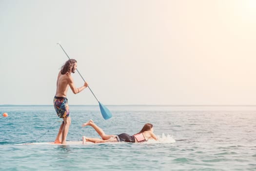 Silhouette of woman standing, surfing on SUP board, confident paddling through water surface. Idyllic sunset or sunrise. Sports active lifestyle at sea or river.