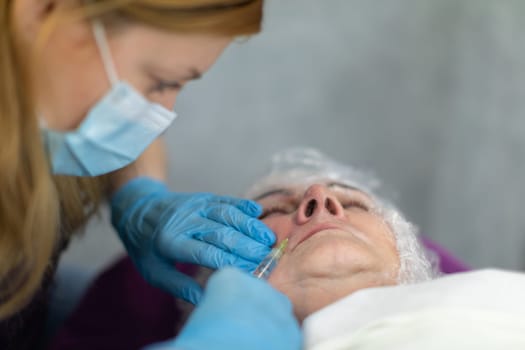 The cosmetologist's face seen in profile. A cosmetologist wears a surgical mask and disposable gloves. Performing mesotherapy in a cosmetology salon.
