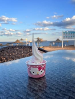 On the table in a cup there is a beautifully decorated delicious creamy fruit ice cream against the background of the sea and the sky with clouds