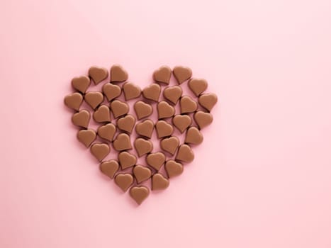 Big heart made of romantic chocolate confections in heart shapes on pastel pink background. Heart of milk chocolate praline sweets, copy space. Top view or flat lay . Valentines Day concept