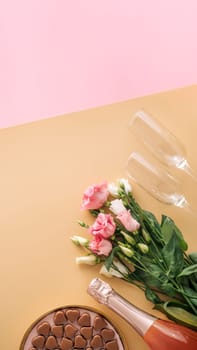 Valentines Day concept on pastel yellow background. Pink champagne bottle,glasses,flowers bouqet and romantic chocolate confections in heart shapes.Copyspace.Champagne beige background.Topview flatlay