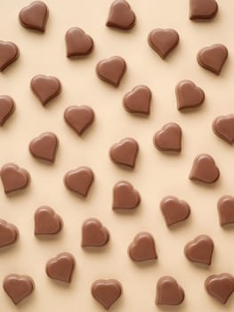 Pattern of romantic chocolate bonbons in heart shapes on pastel yellow background. Pattern of heart milk chocolate sweets or candies on champagne beige background. Top view or flat lay. Vertical