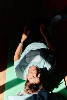 In a sunlit space, a senior woman gracefully practices rejuvenating yoga, focusing on neck, back, and leg stretches, embodying serenity and well-being.