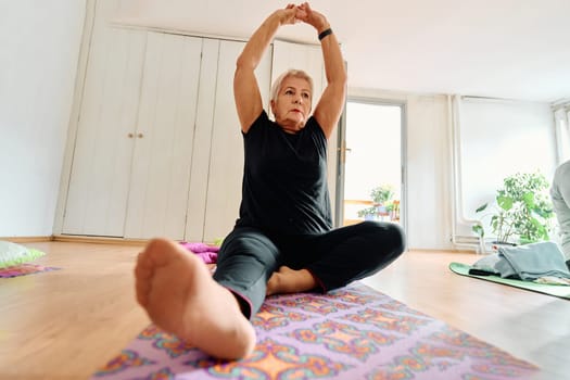 An elderly woman gracefully engages in various yoga poses, stretching her limbs and finding serenity in a modern sunlit space under the guidance of a trained instructor, embodying the essence of active and mindful aging.