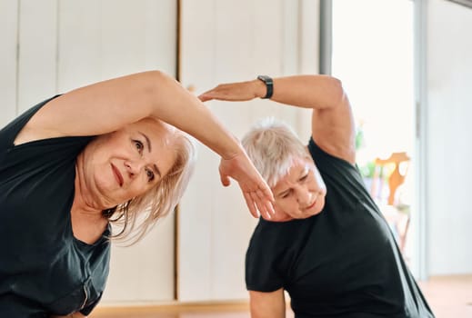 A group of senior women engage in various yoga exercises, including neck, back, and leg stretches, under the guidance of a trainer in a sunlit space, promoting well-being and harmony.