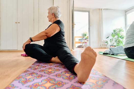 An elderly woman gracefully engages in various yoga poses, stretching her limbs and finding serenity in a modern sunlit space under the guidance of a trained instructor, embodying the essence of active and mindful aging.