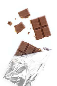 Bar of milk chocolate and almonds in a silver foil, partially unwrapped. On white background, pieces of chocolate.