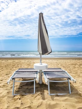 Two sunbeds and an umbrella closed in front of the sea at the end of summer in a deserted beach.