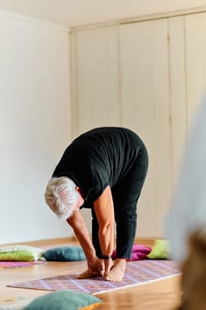 In a sunlit space, a senior woman gracefully practices rejuvenating yoga, focusing on neck, back, and leg stretches, embodying serenity and well-being.