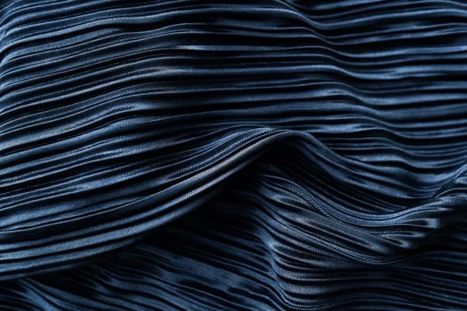 A dark blue pleated fabric with a shiny texture and intricate folds. It has an artistic feel due to the play of light and shadow on the folds