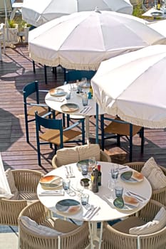 France. Nice. A cafe on the beach, served tables await visitors. Beach with sun loungers, white umbrellas and palm trees against the backdrop of the beauty of the sea
