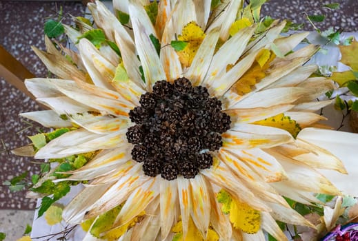 A large sunflower is made of corn cones and leaves.