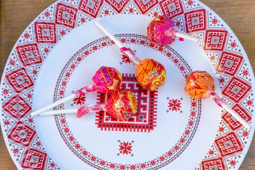 Candies on a plate with Ukrainian ornament. Chupa-Chups on a plate. Ukraine, Vinnytsia, 02.06.2023