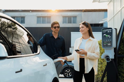 Eco-friendly conscious family couple recharging EV vehicle from home charging station. EV electric car technology utilized as alternative transportation for future sustainability. Expedient