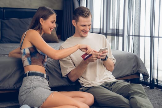 Young couple sit in the home bedroom using online payment app and digital wallet on smartphone to pay with credit card. E commerce shopping and modern purchasing via mobile internet. Unveiling