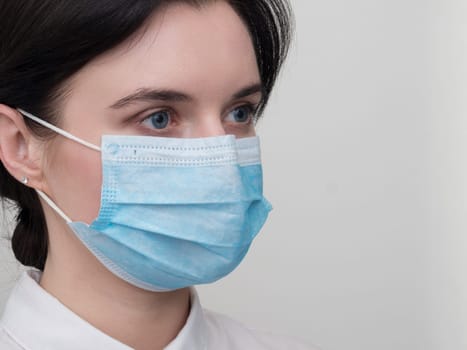 Portrait of a young European woman in a protective disposable medical mask. Concept of caronavirus Cavid 19 and human quarantine. Girl in a mask on a white wall. Masked medical worker