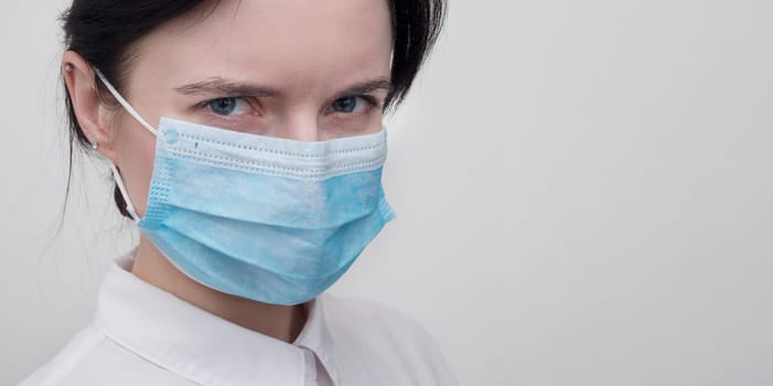 Portrait of a young European woman in a protective disposable medical mask. Concept of caronavirus Cavid 19 and human quarantine. Girl in a mask on a white wall. Masked medical worker