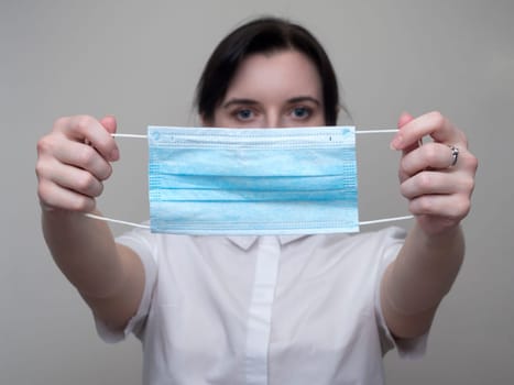 Woman holds out a medical mask in her hands. Coronavirus COVID-19