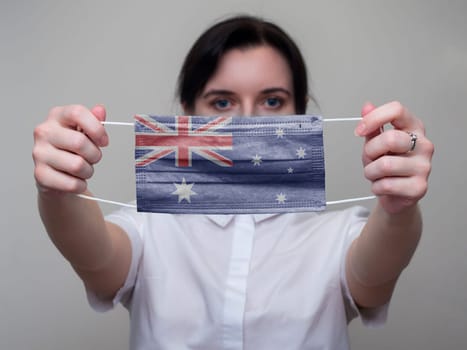 Woman holds out in her hands a medical mask with the image of the flag of Australia. Coronavirus COVID-19