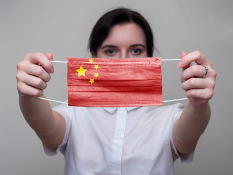 Woman holds out a medical mask with the image of the flag of China. Coronavirus COVID-19