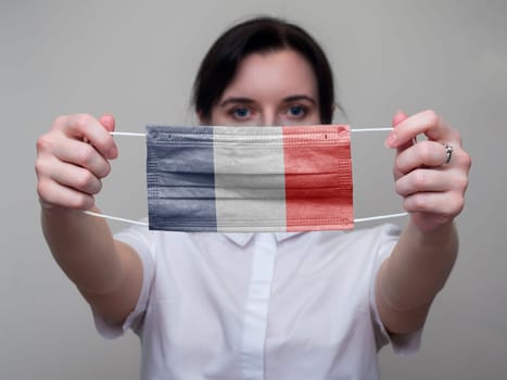 Woman holds out in her hands a medical mask with the image of the flag of France. Coronavirus COVID-19