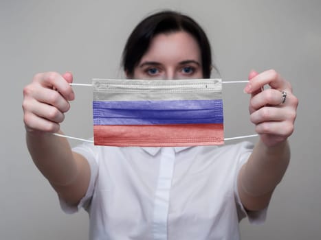 Woman holds out a medical mask with the image of the flag of Russia in her hands. Coronavirus COVID-19