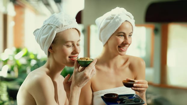 Couple of beautiful woman interested in homemade facial masks while sitting at spa salon. Attractive woman in white towel enjoy herbal masks with her friend surrounded by nature. Tranquility.