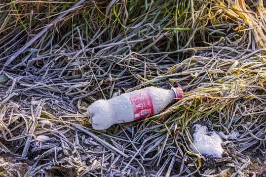 A plastic bottle frozen with ice crystals lies in nature in a meadow in winter