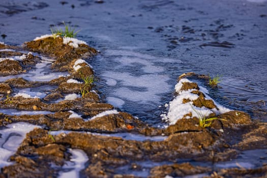 Traces in the dirt of a dirt road next to a field with frozen water in a puddle, in winter