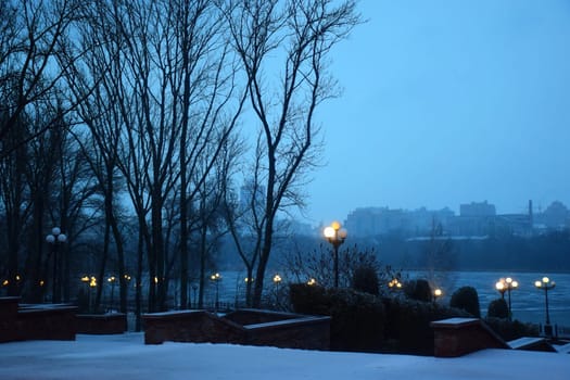 Winter park in the evening covered with snow with a row of lamps