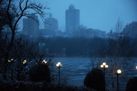 Winter park in the evening covered with snow with a row of lamps