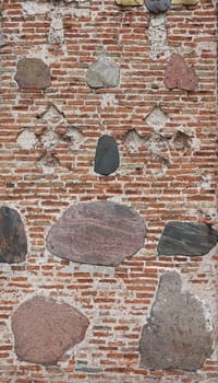 Abstract background from a wall with bricks and stones. Old fortress wall of red brick interspersed with large cobblestones