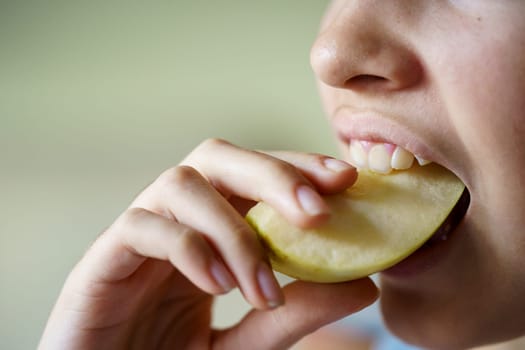 Closeup of anonymous teenage girl eating fresh apple slice at home