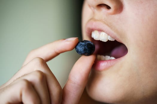 Crop unrecognizable teenage girl about to eat delicious organic blueberry at home