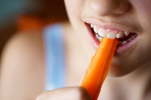 High angle closeup of crop anonymous teenage girl biting fresh healthy carrot slice at home