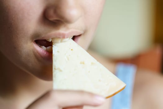 Closeup of crop anonymous young girl eating yummy cheese slice at home