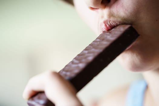 Closeup of crop anonymous young girl eating chocolate protein bar at home